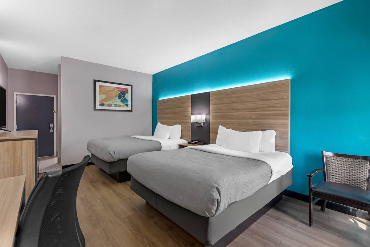 A hotel room with two beds, a desk, a chair, and a painting on the wall.