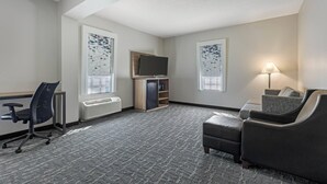 Una habitación de hotel con escritorio, silla de oficina, sofá, televisor y lámpara.