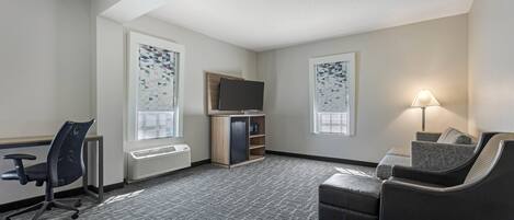 A hotel room with a desk, office chair, sofa, TV, and a lamp.