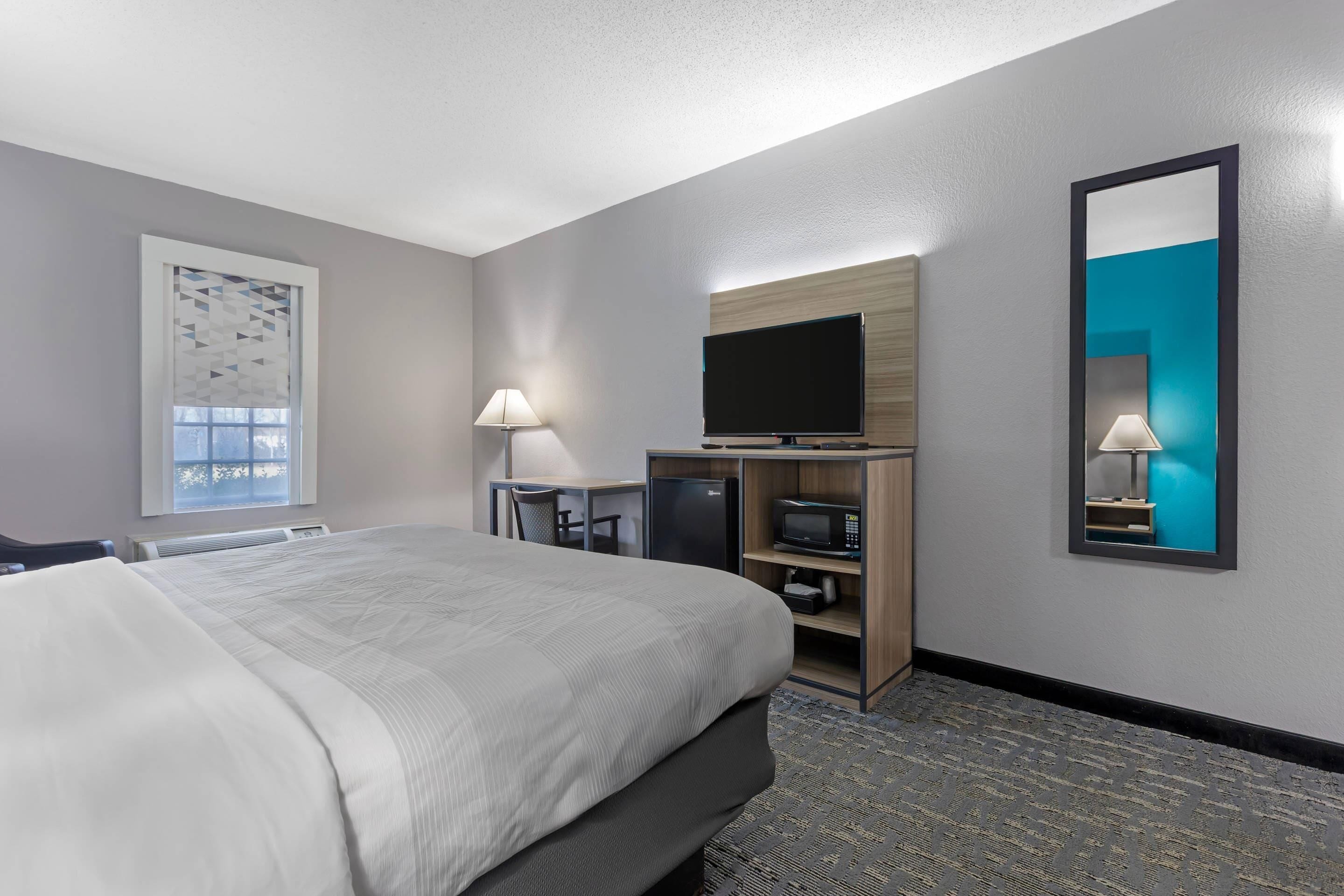 A hotel room with a large bed, a desk with a computer and TV, a mirror, and a window with a view.