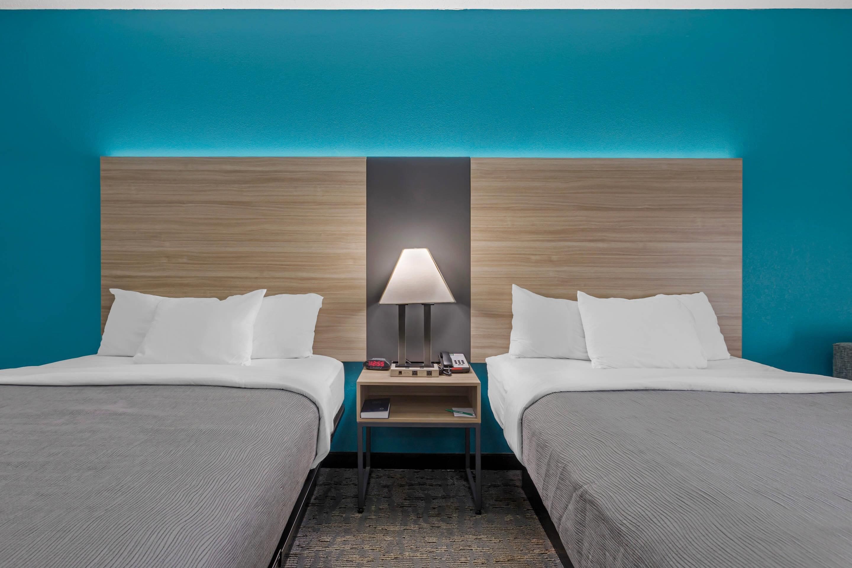 Quarto de hotel com duas camas, uma mesa de cabeceira com abajur, telefone e uma pequena mesa.