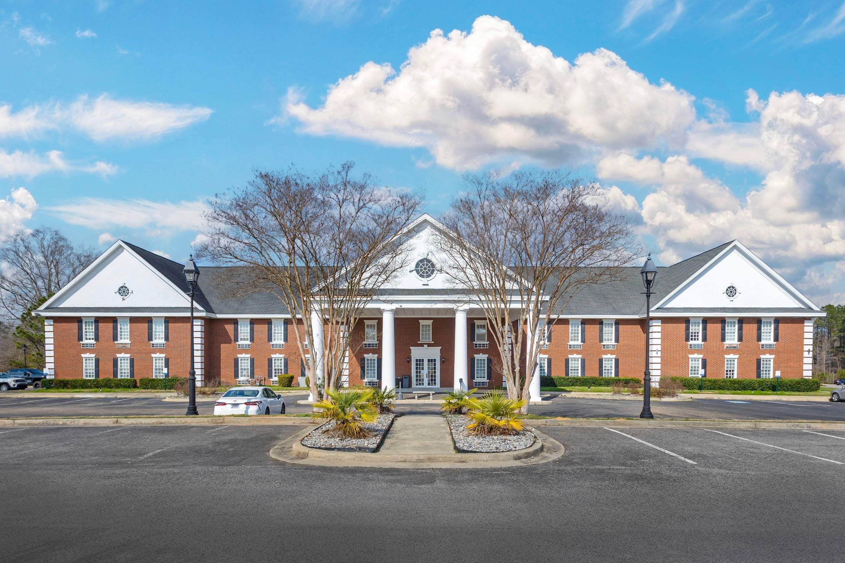 A two-story brick building with a central entrance, columns, and a symmetrical facade.