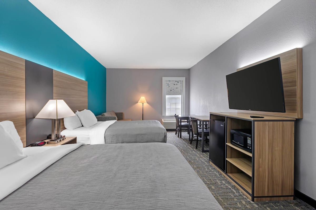 A hotel room with two beds, a desk with a chair, a television, and a microwave.