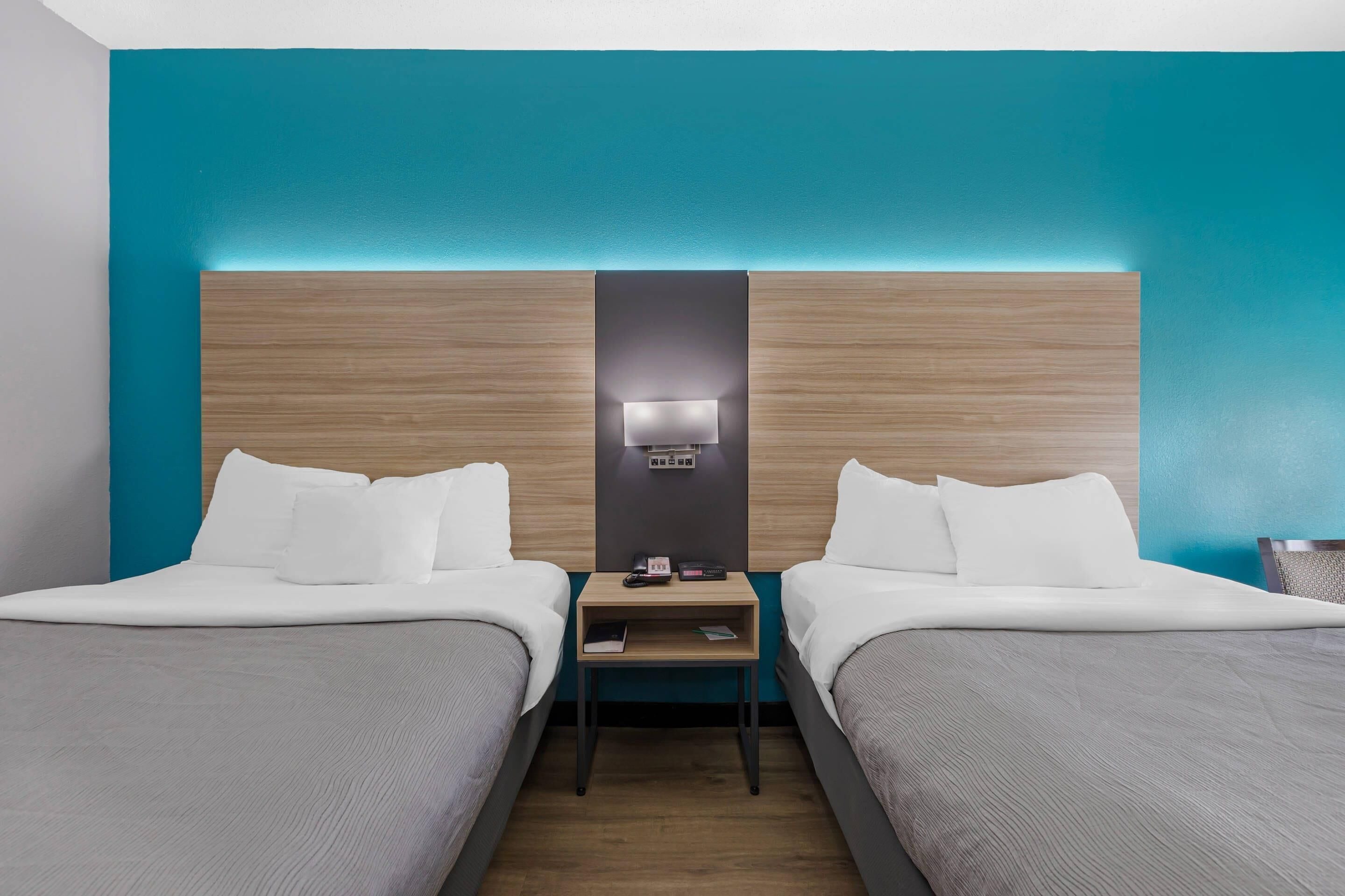 A hotel room with two beds, a nightstand with a lamp, and a wall-mounted phone.