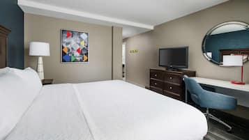 A hotel room with a large bed, a desk with a chair, a television, a mirror, and a wall-mounted painting.