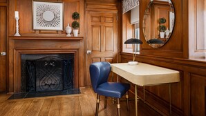 A room with a wooden paneled wall, a fireplace, a blue chair, a table, and a mirror. - Hampton Inn Washington, D.C./White House (Washington)