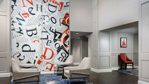 A modern lobby with two grey armchairs, a patterned wall, and a red chair in the background. - Hampton Inn Washington, D.C./White House (Washington)