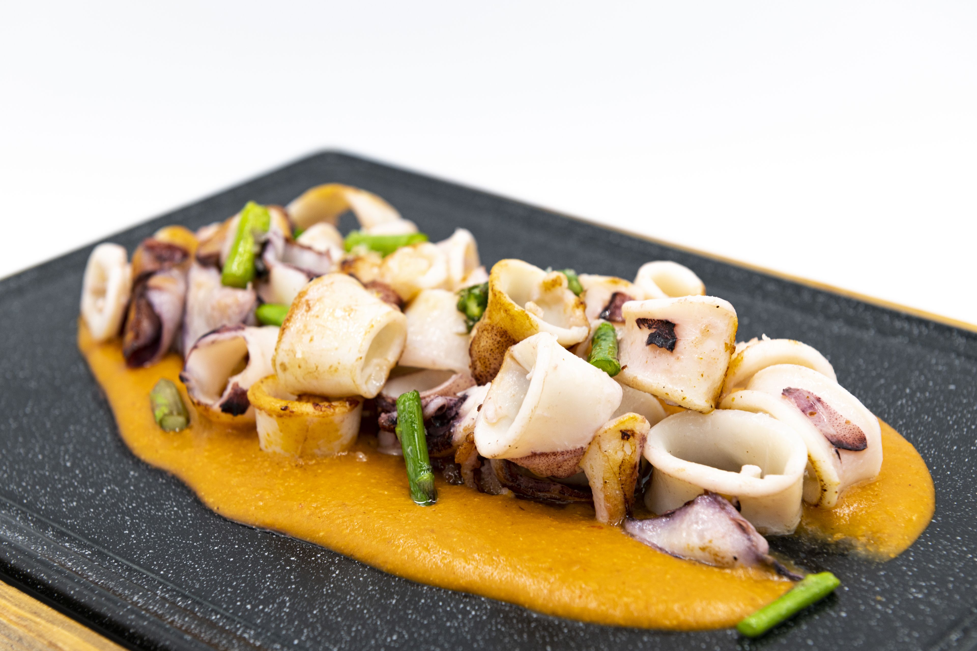 Un plato de pulpo con salsa cremosa y verduras verdes sobre un plato negro.