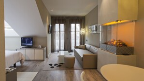 Une chambre d’hôtel moderne équipée d’un lit, d’un canapé, d’une télévision, d’une cheminée et d’une grande fenêtre avec des rideaux.