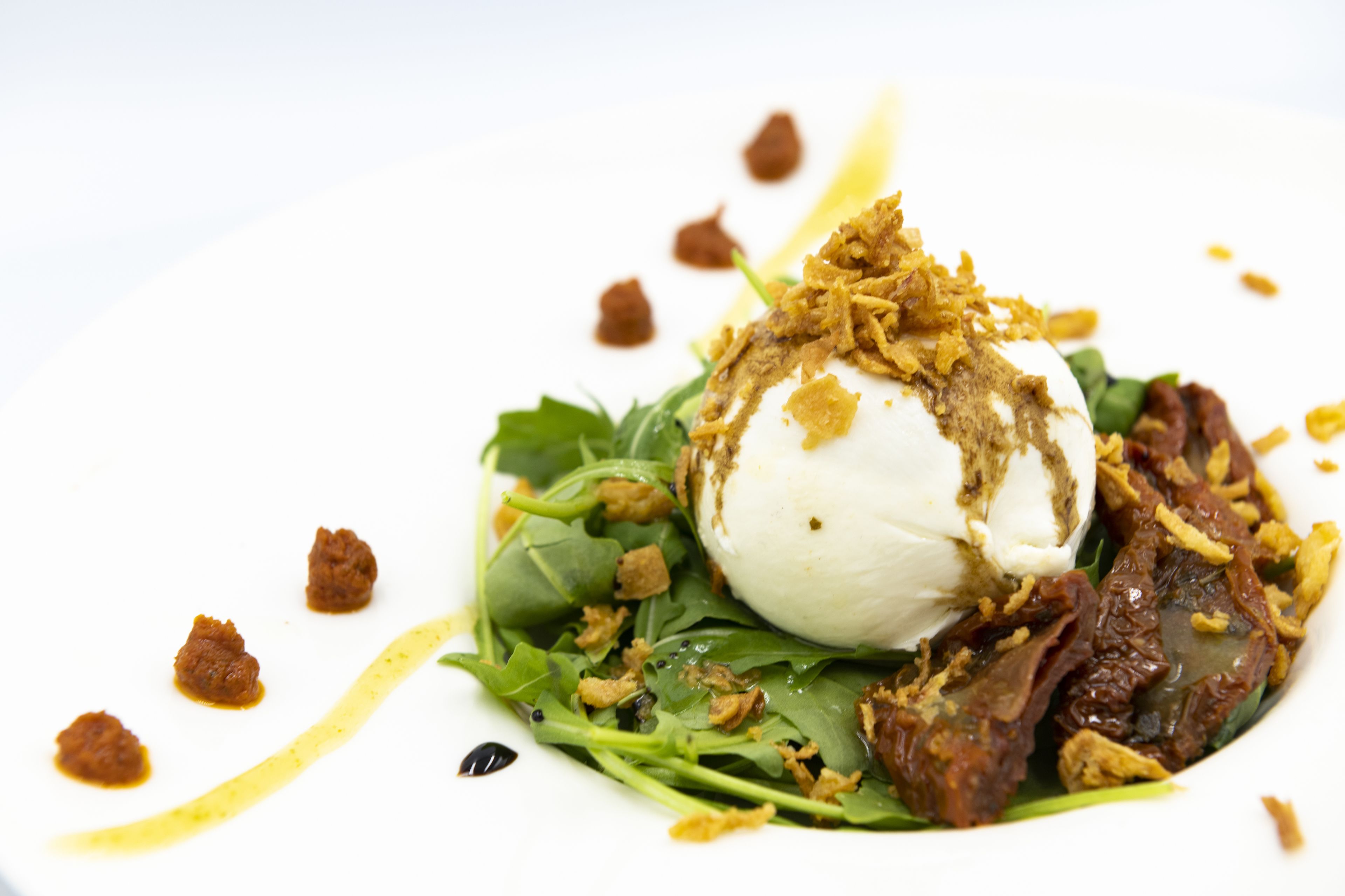 Un plato con una porción de helado sobre una base de hojas verdes y ingredientes crujientes.