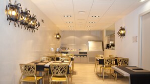 Un espace de repas moderne avec une longue table et des chaises, une cuisine en arrière-plan et des appliques murales décoratives.