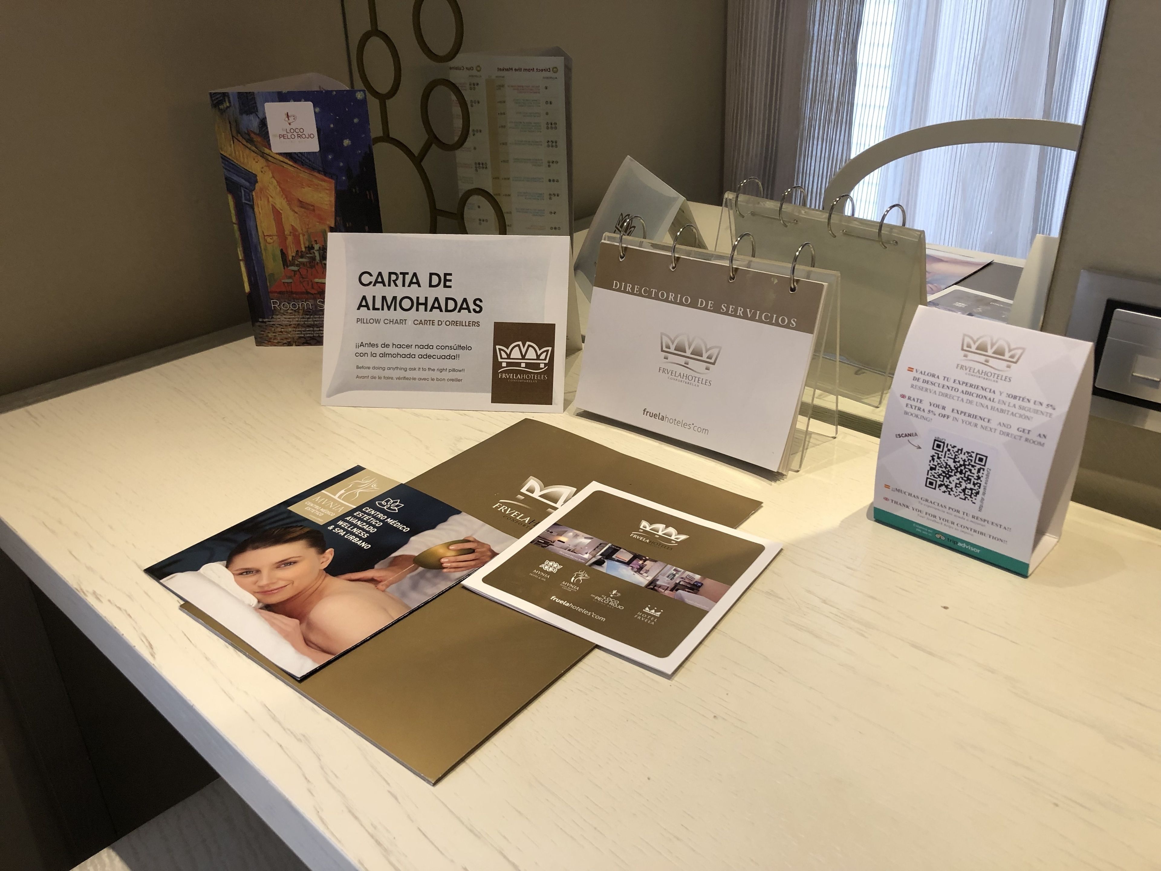 Mostrador de recepción de hotel con folletos informativos, cuadro de almohadas y un código QR para atención al cliente.
