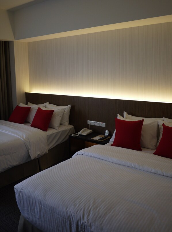 A hotel room with two beds, each with white bedding and red pillows, a bedside table with a phone and a remote control, and a wall-mounted light above the beds. - Emperor Hotel (Taipei)