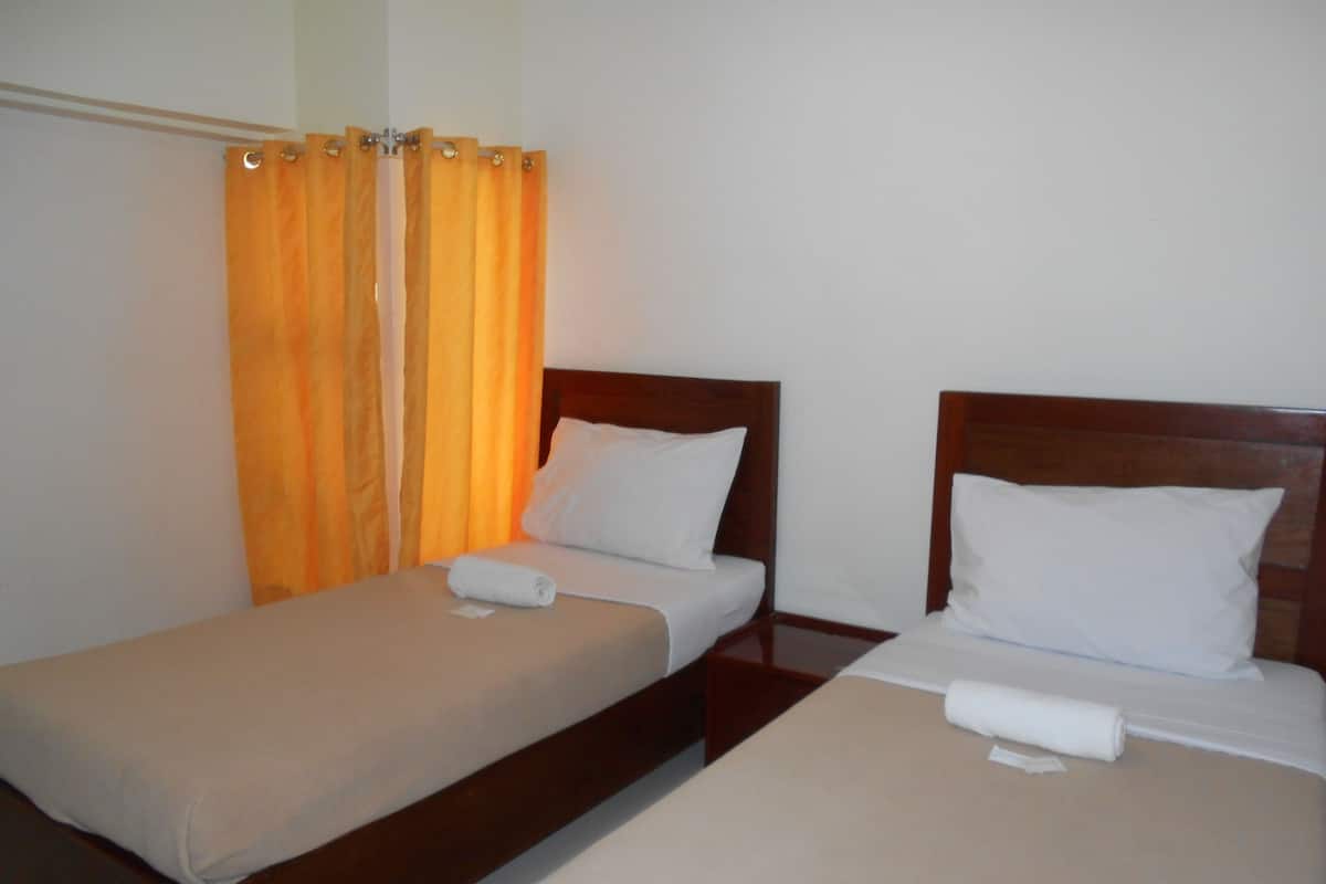 Two single beds with wooden headboards and white linens, separated by a small table.