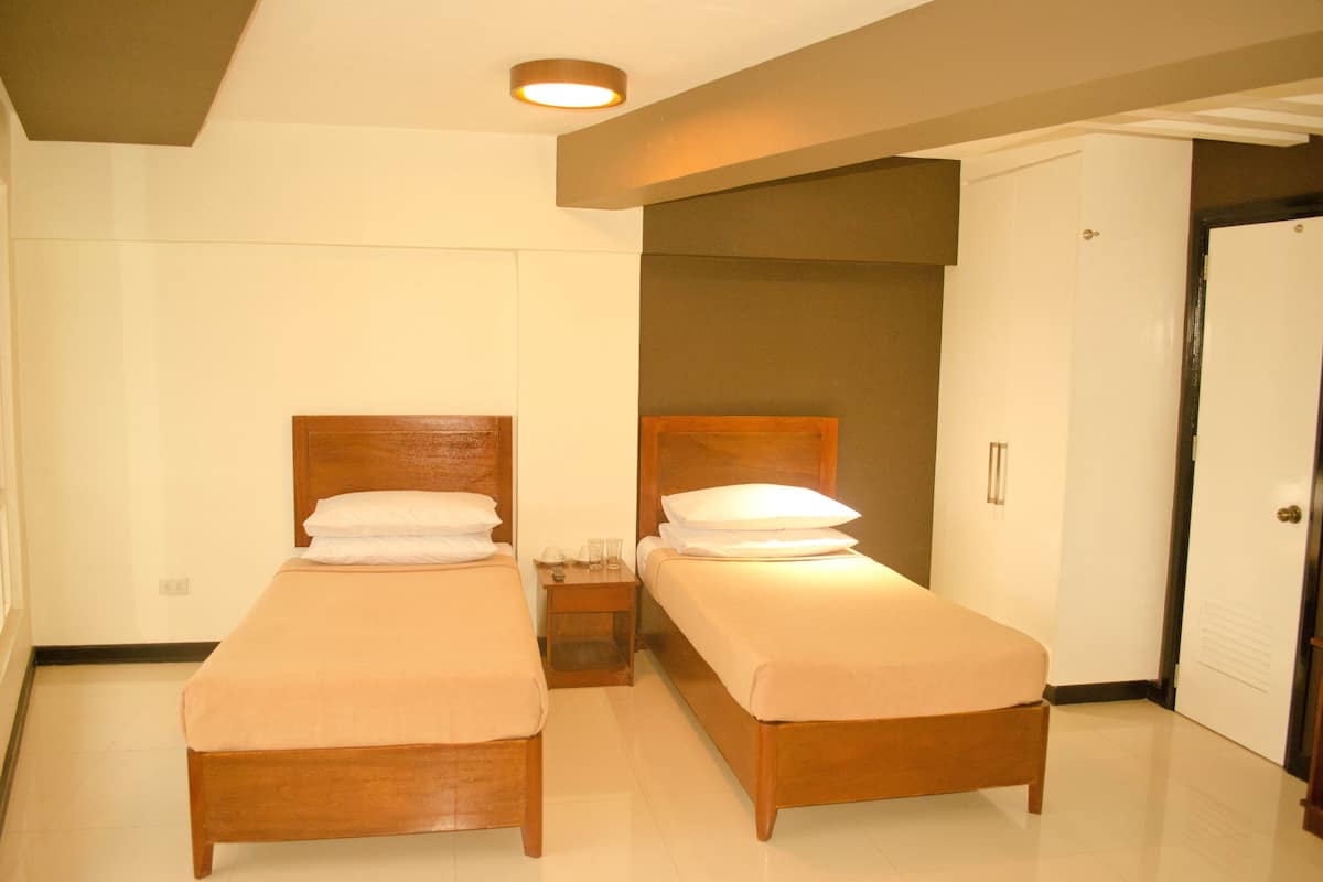 A hotel room with two single beds, a nightstand, a door, and a ceiling light.