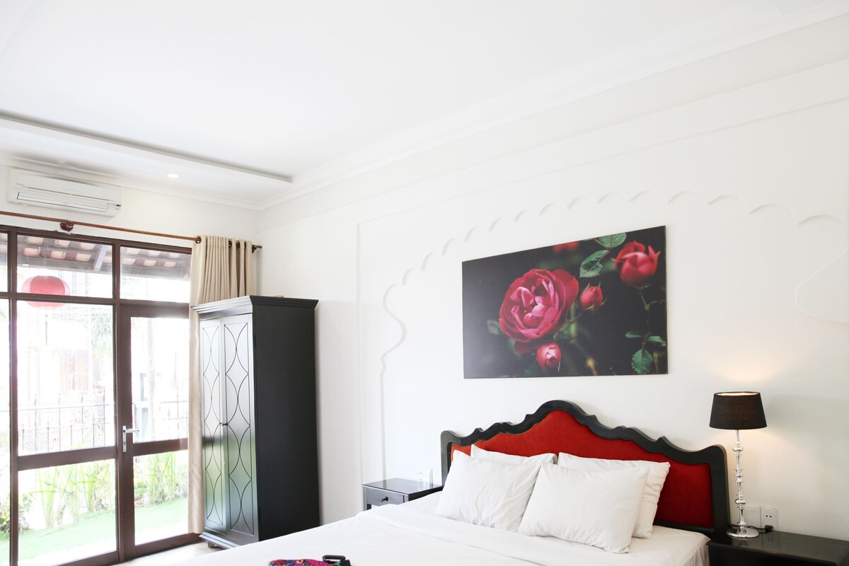 A hotel room with a bed, a nightstand, a lamp, a wardrobe, and a large window with curtains.