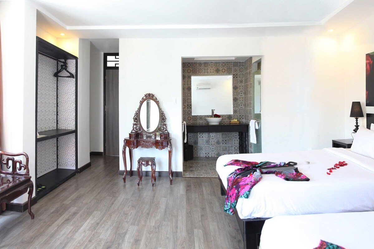 A hotel room with a bed, a desk, a chair, a mirror, and a bathroom visible through an open door.