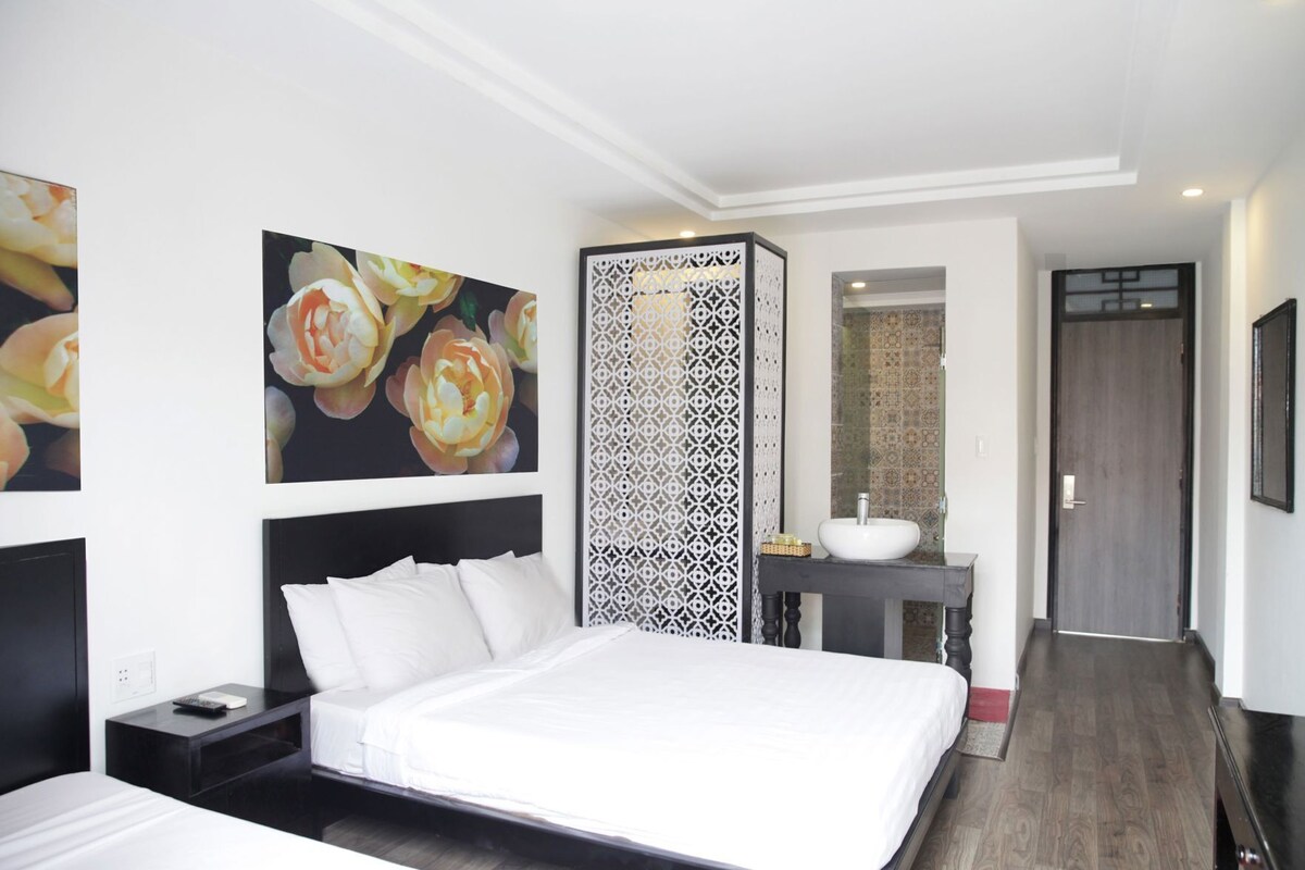 A hotel room with a bed, a nightstand, a wall-mounted TV, a decorative screen, a bathroom with a sink, and a door.