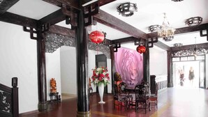A traditional interior with ornate wooden pillars, a floral centerpiece, and a pink floral backdrop. - Thanh Binh II (Da Nang)