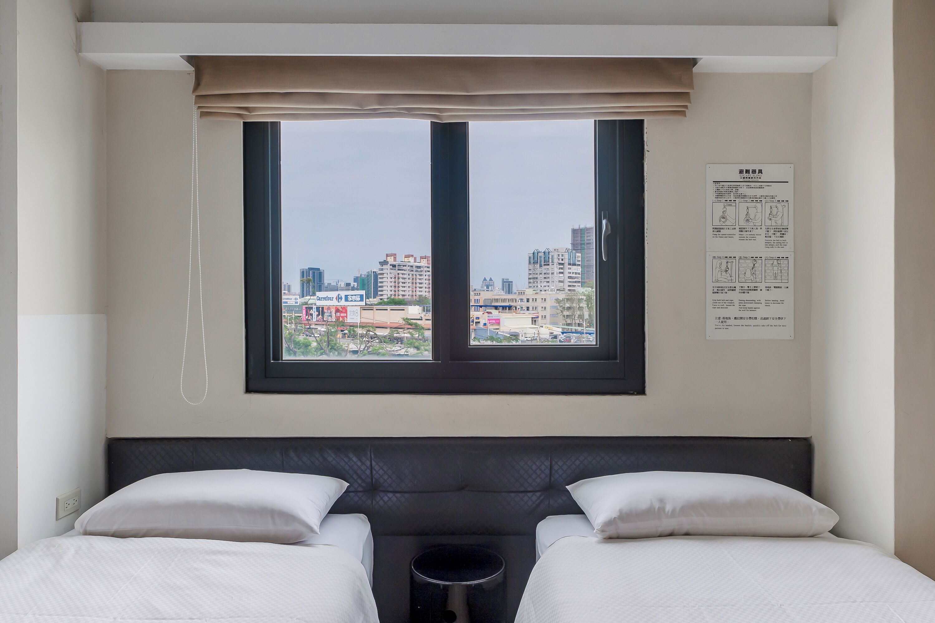 A hotel room with a large window, a bed with white bedding, a small bedside table, and a city view.