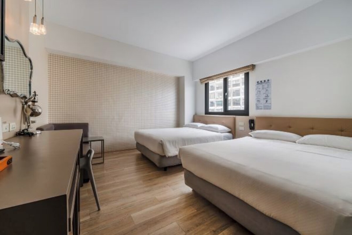 A hotel room with two beds, a desk, and a chair.