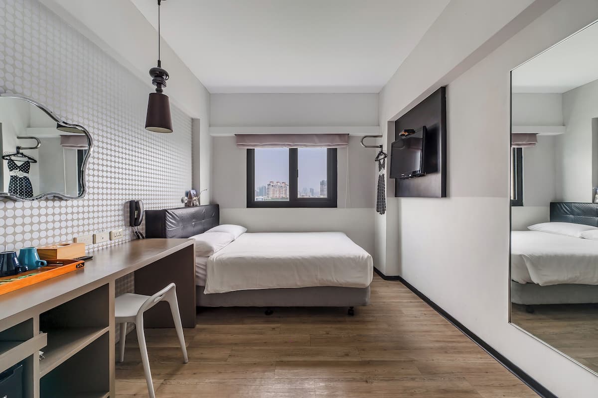 Une chambre d’hôtel moderne équipée d’un lit, d’un bureau, d’une chaise et d’un grand miroir.