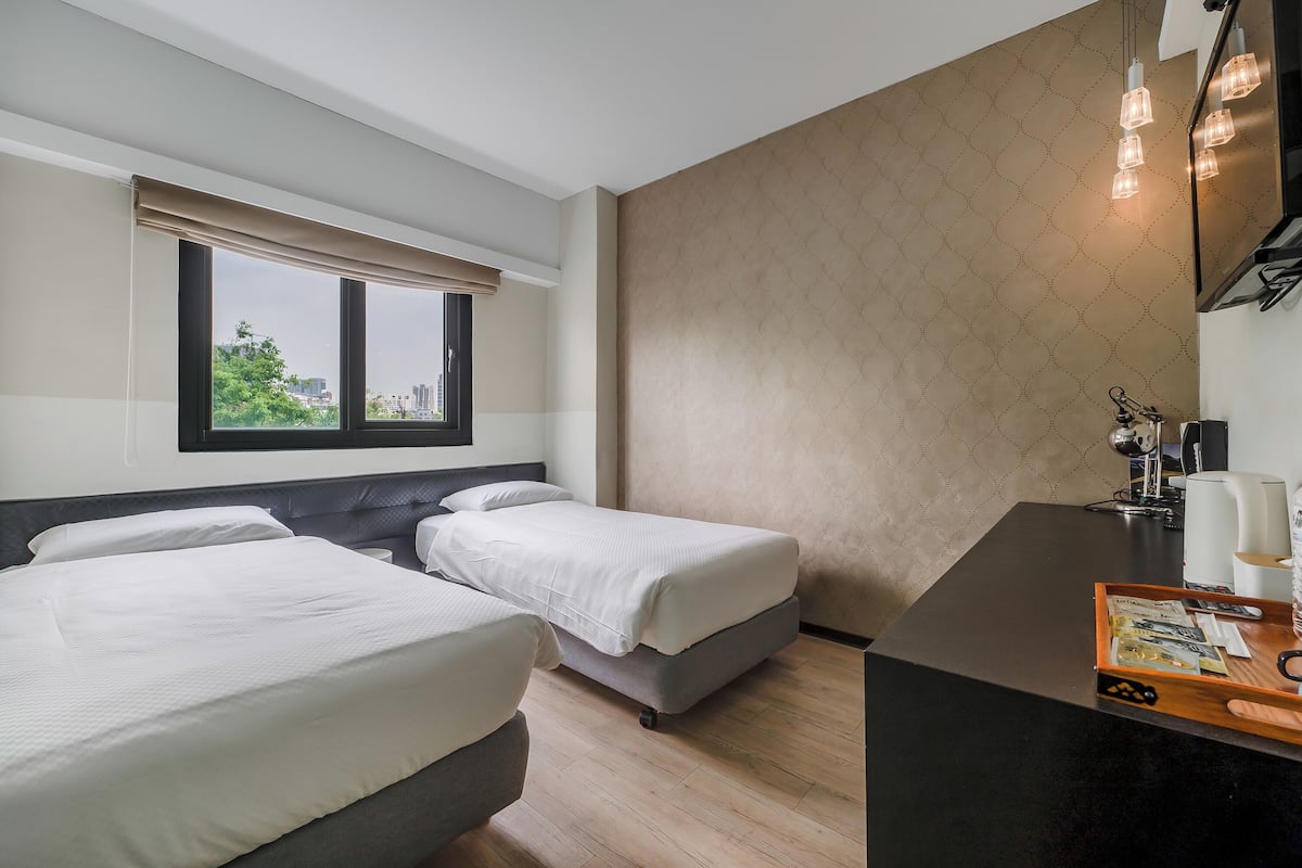 Une chambre d’hôtel avec deux lits simples, un bureau avec une chaise, une fenêtre donnant sur la ville et un mur décoré d’un motif.