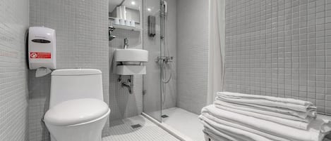 A modern bathroom with a toilet, a glass-enclosed shower, and a stack of white towels.