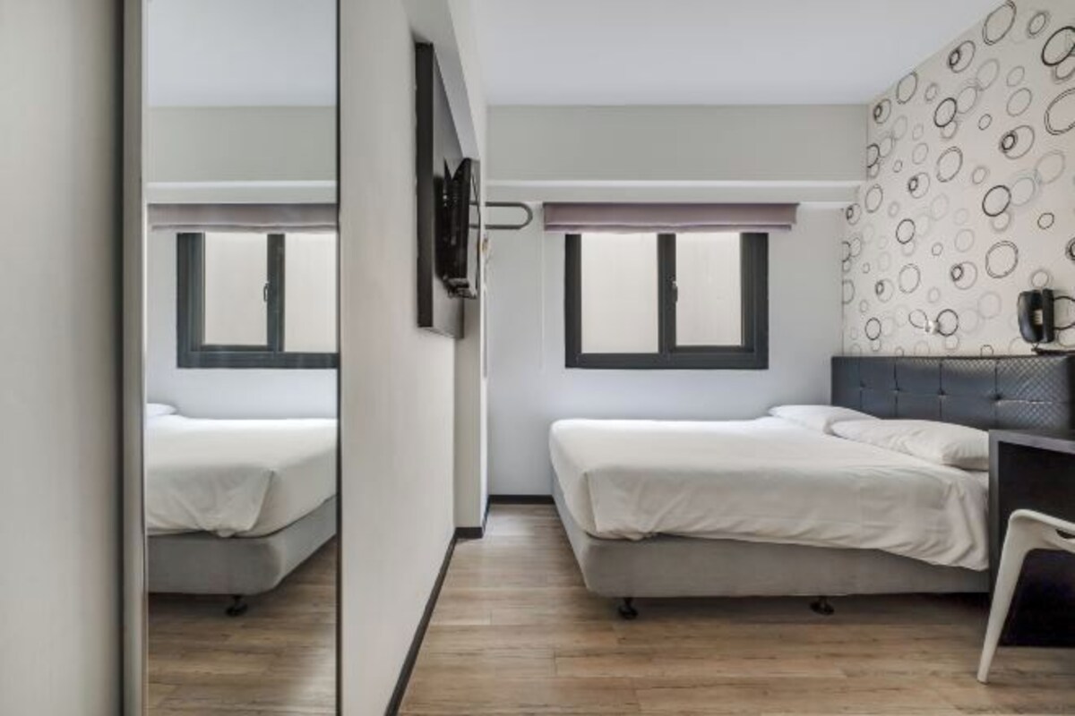 A modern bedroom with two beds, a TV, and a patterned wall.