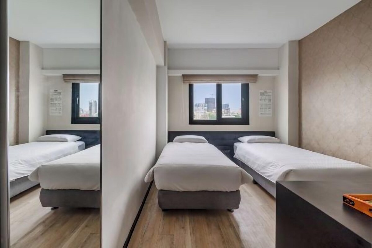 A hotel room with two single beds, a large window with a city view, and a wooden floor.