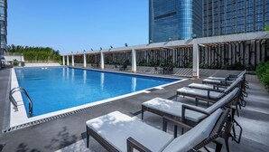 Una piscina en la azotea con sillones de descanso y vistas a edificios altos.
