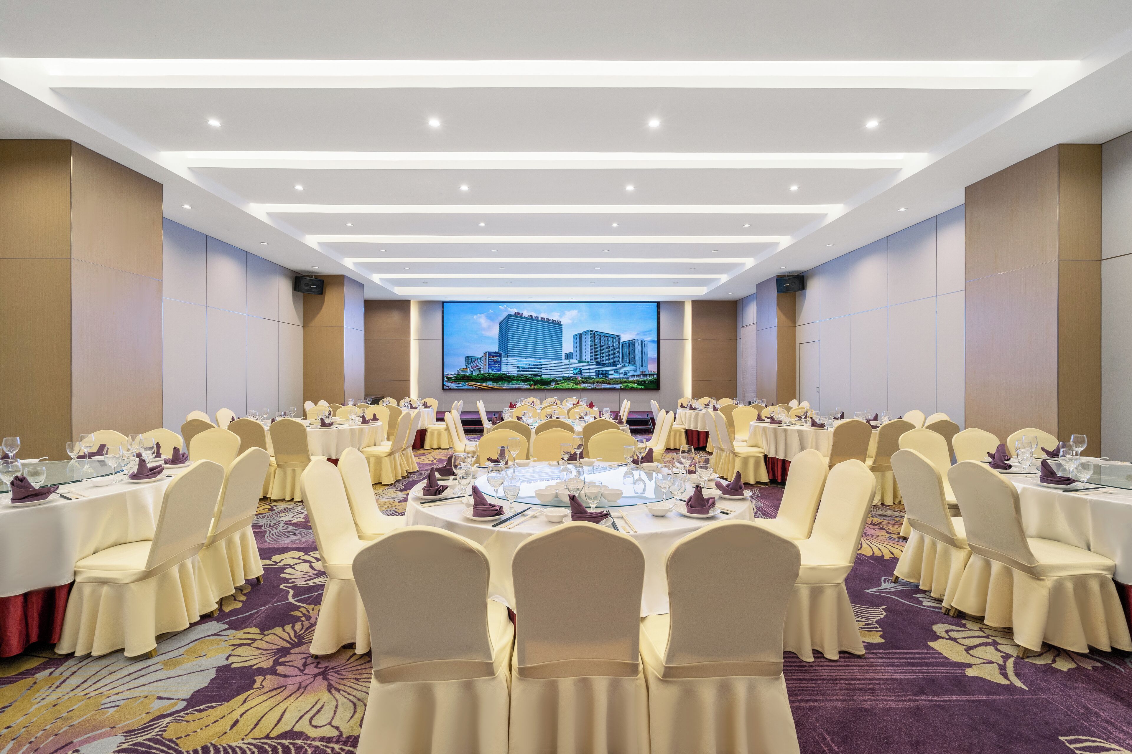 A conference room with round tables, white chairs, and a large screen displaying a cityscape.