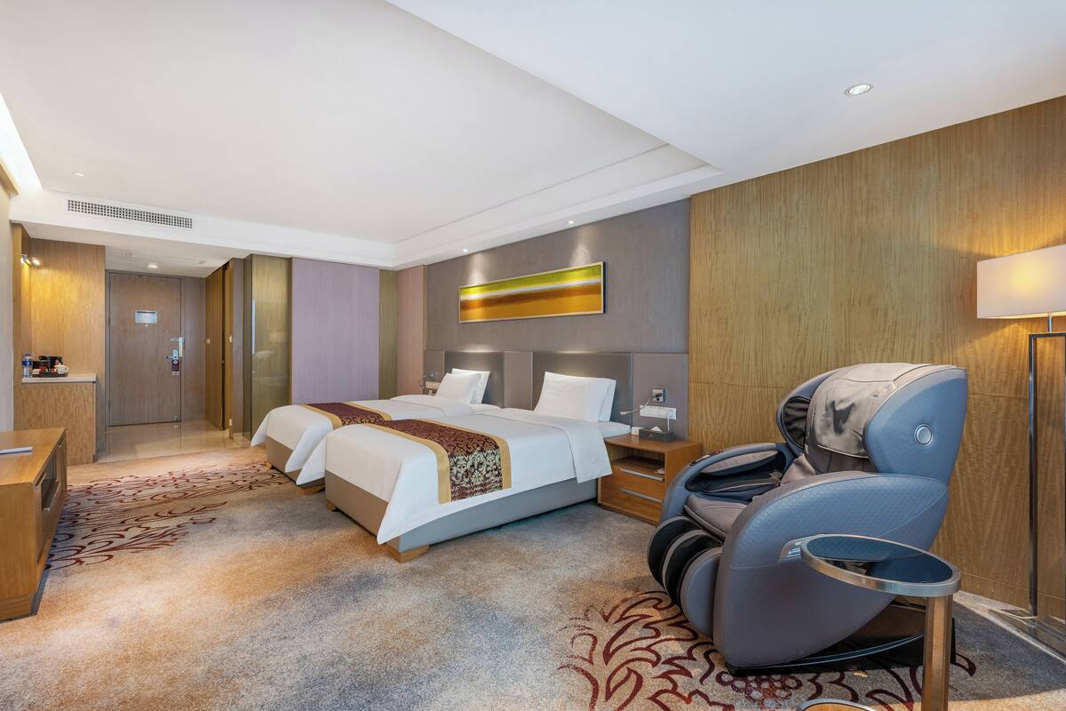 Habitació d'hotel amb dos llits, una cadira de massatge, un escriptori i una finestra gran.