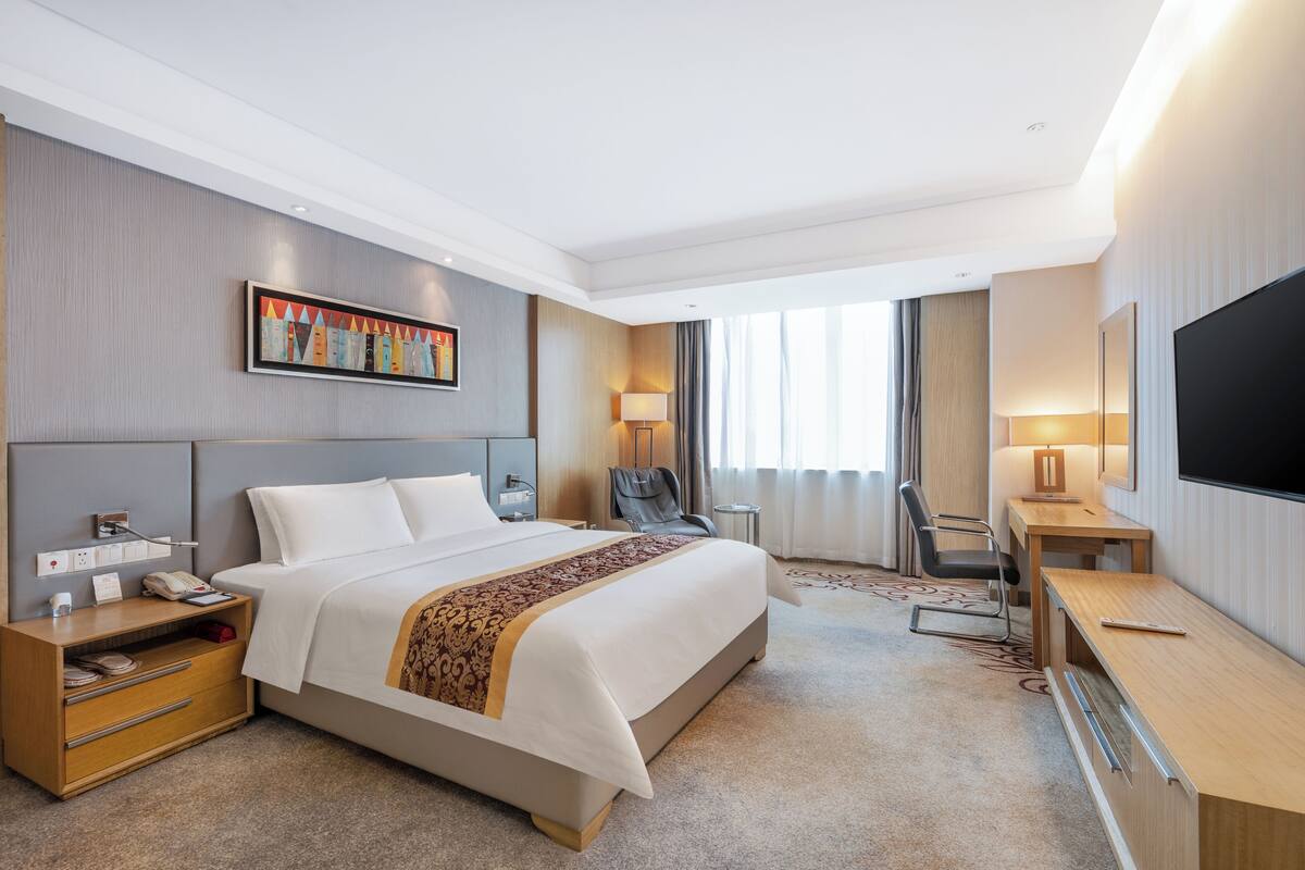 Habitació d'hotel amb un llit gran, una taula de treball, una cadira, un televisor i un quadre a la paret.