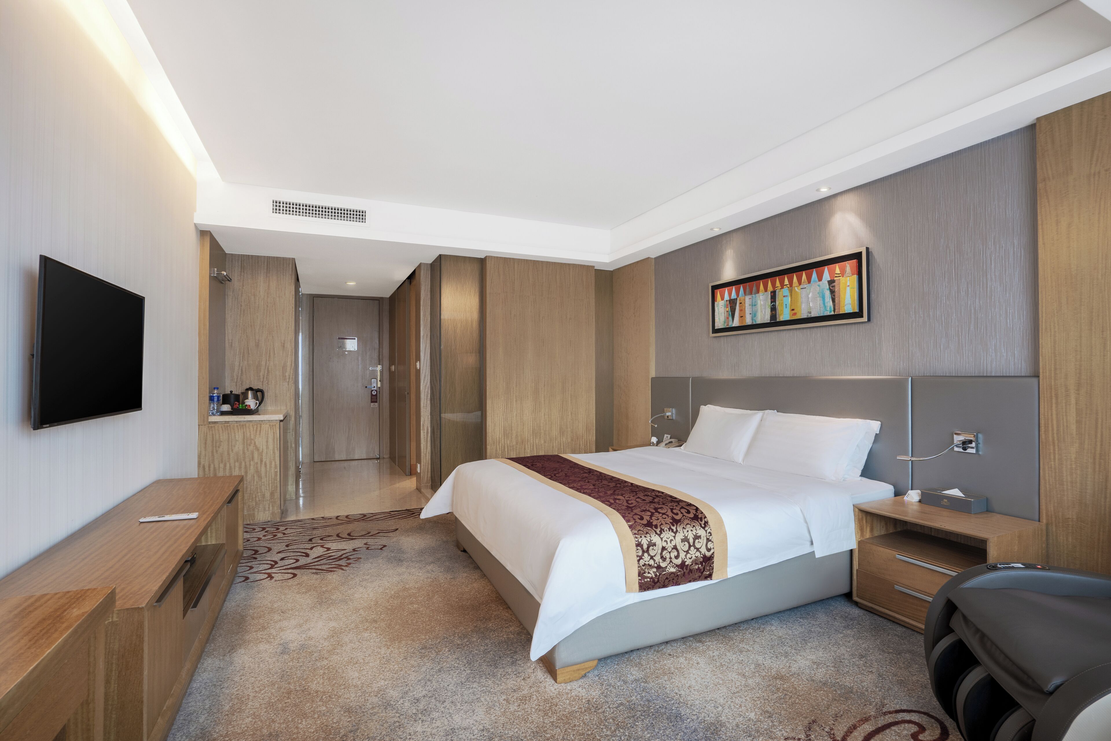 A modern hotel room with a large bed, a flat-screen TV, a wooden desk, and a small seating area.