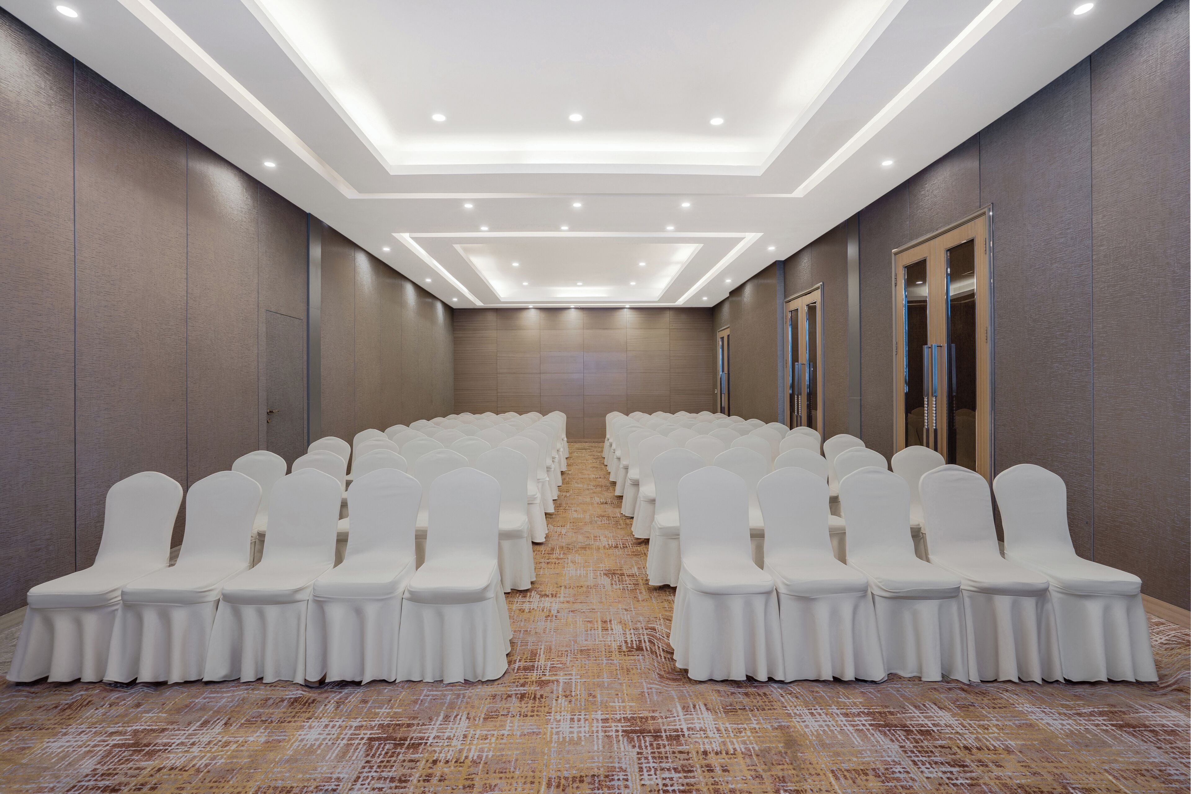 Una sala conferenze con file di sedie bianche e pavimento rivestito di moquette.