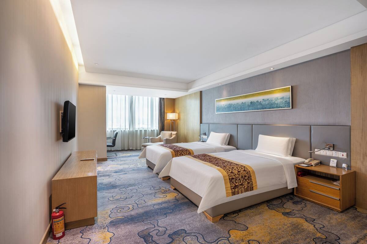 Habitació d'hotel amb dos llits, un escriptori, una cadira, un televisor, un extintor i un quadre a la paret.