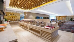 Un moderno vestíbulo de hotel con un largo mostrador de recepción, zona de buffet y área de descanso.