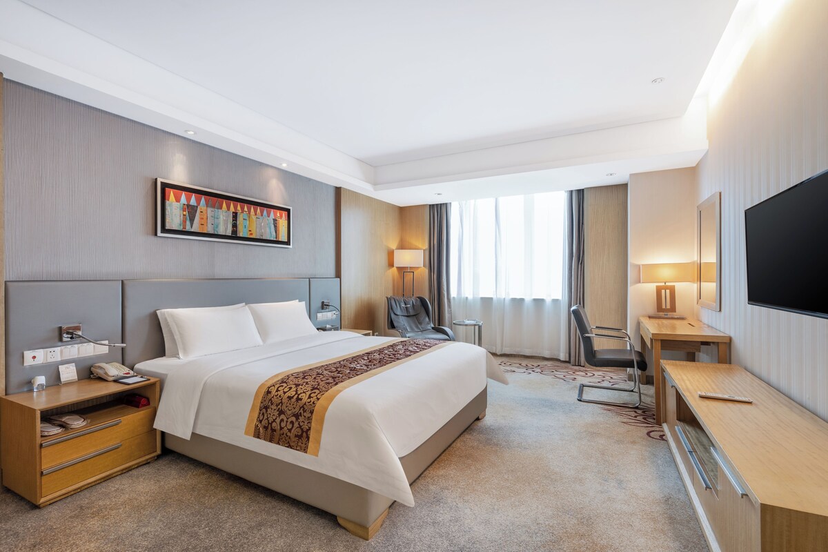 Une chambre d’hôtel avec un grand lit, un bureau, une chaise, une télévision et un tableau au mur.