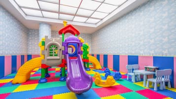 Kids can play safely in this enclosed play area featuring a slide, climbing structure, and play toys, with seating for adults nearby.