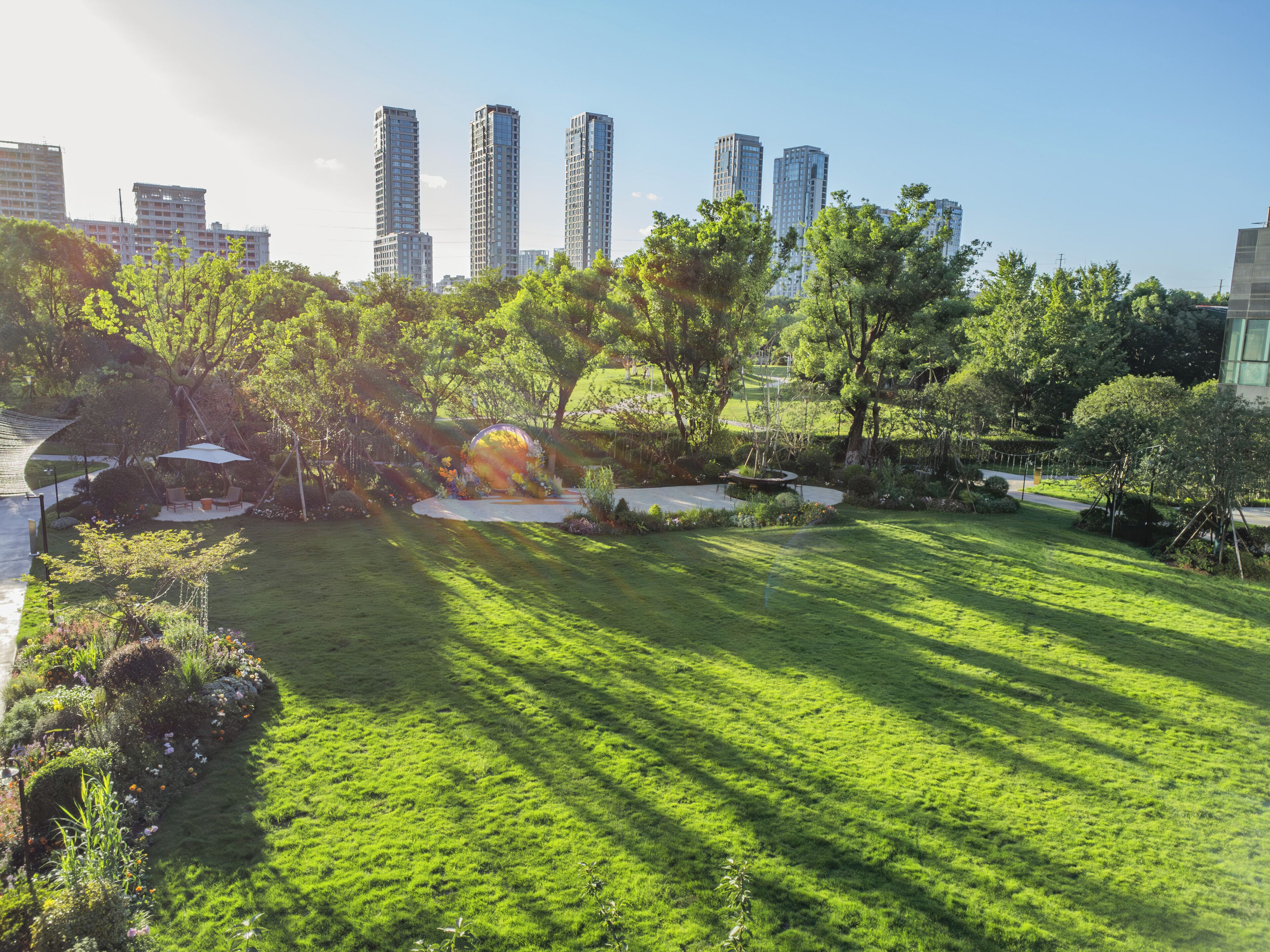 A park with a circular flower bed, a seating area, and tall buildings in the background.