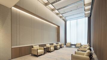 A modern hotel lobby with a long row of leather armchairs, a high ceiling with recessed lighting, and large windows.