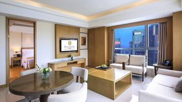 A modern hotel room with a dining area, a sofa, a TV, and a city view.
