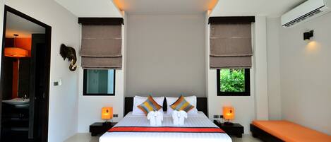 Una habitación de hotel moderna con una cama grande, dos mesitas de noche, un banco y vistas al exterior con vegetación.