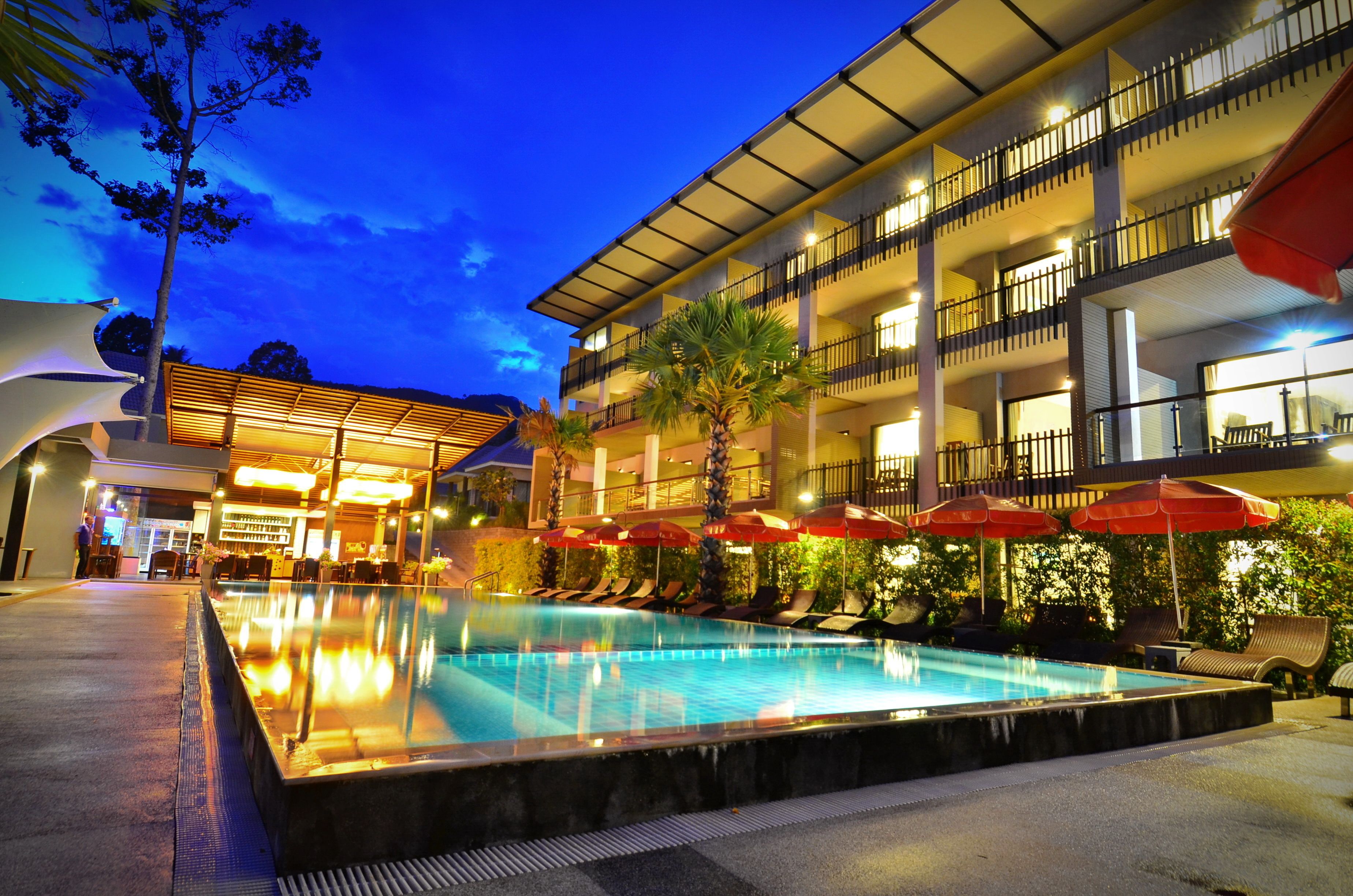 A hotel with a swimming pool, outdoor seating, and a multi-story building with balconies.