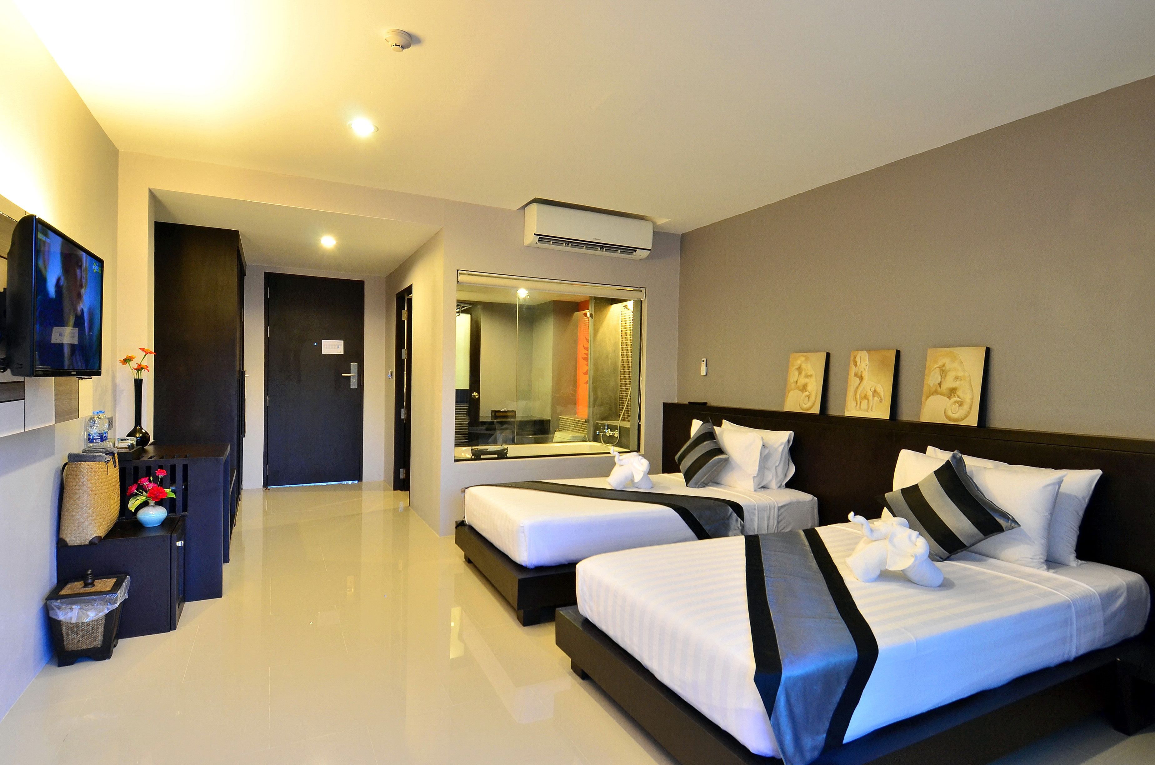 A modern hotel room with two beds, a flat-screen TV, a vanity with a mirror, and a small seating area with a vase and decorative items.
