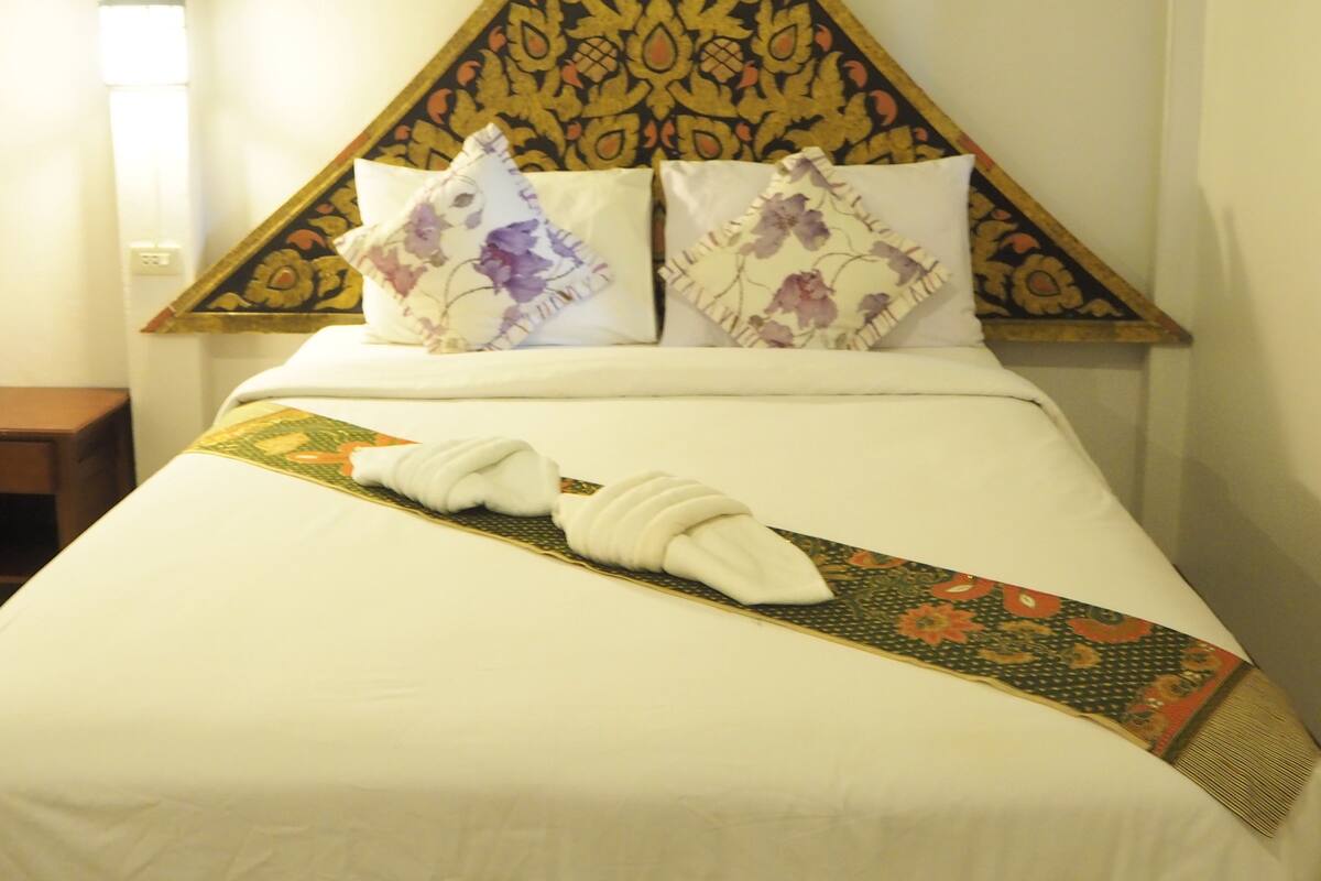Habitación de hotel con una cama, dos almohadas de estampado floral, una manta blanca y un cabecero decorativo con diseño geométrico.