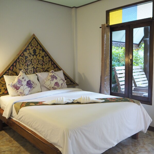 A neatly made bed with white linens and floral pillows, a wooden headboard, and a view of greenery through a window. - Khao Sok Green Valley Resort (Phanom)