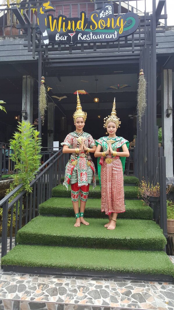 A bar and restaurant entrance with two individuals in traditional attire standing on a green artificial grass step. - Khao Sok Green Valley Resort (Phanom)