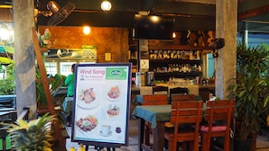 Un restaurante con zona de bar, mesas y sillas de madera, y un letrero que anuncia 'Wind Song Bar & Restaurant'.